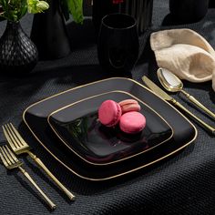 a black plate topped with pink macaroons next to gold forks and silverware