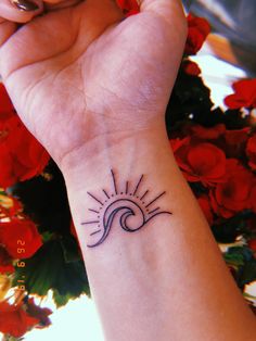 a woman's wrist with a small sun and wave tattoo on it