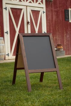 a chalkboard sign in front of a red barn with an open door on the grass