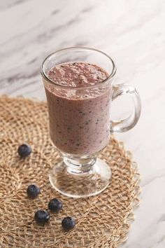 a glass mug filled with blueberries on top of a table next to a straw mat