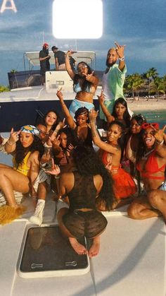 a group of women sitting on top of a boat in front of the ocean with their hands up