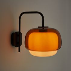 a wall light that is on the side of a wall with an orange glass shade