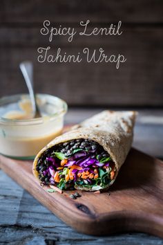 a wrap filled with black beans, carrots and lettuce next to a bowl of dressing