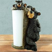 three black bears sitting on top of a toilet paper holder next to a white roll