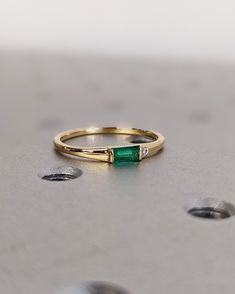 a gold ring with a green stone in the middle on top of a metal surface