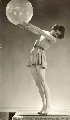 an old photo of a woman holding a large balloon in her hand while standing on a pedestal