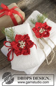 two wrapped presents with red crocheted flowers on them