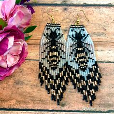 two pairs of beaded earrings sitting on top of a wooden table next to flowers