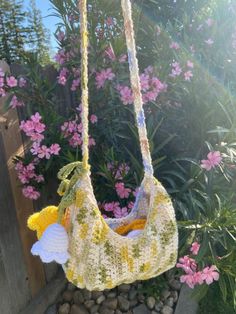 a crocheted bag hanging from a rope in front of some pink and white flowers