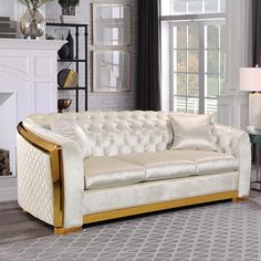 a white and gold couch in a living room with a fire place, fireplace and windows