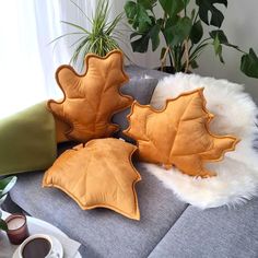 three leaf shaped pillows sitting on top of a couch next to a potted plant