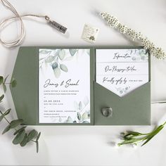 the wedding stationery is laid out with greenery