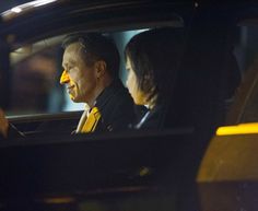 two people sitting in the back seat of a car, one is wearing a yellow tie