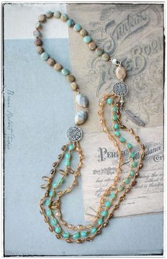 two necklaces with beads and charms on top of a piece of paper next to a postcard