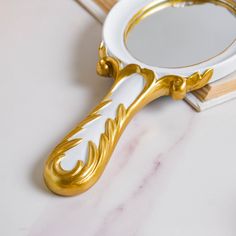 a gold and white vanity mirror sitting on top of a counter next to a brush