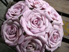 a bouquet of pink roses sitting on top of a wooden bench covered in book pages