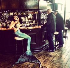 a woman dressed as a mermaid sitting at a bar