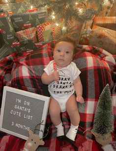 a baby sitting on top of a blanket next to a christmas tree