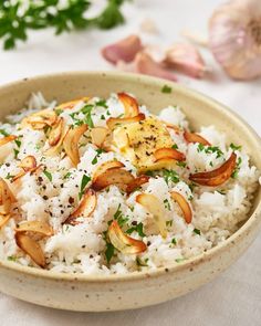 a bowl filled with rice and mushrooms on top of a table next to garlic florets