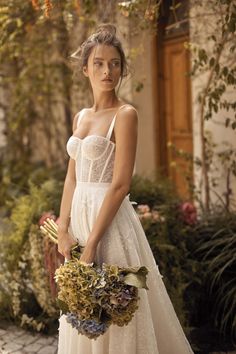 a woman in a white dress is holding a flower bouquet and posing for the camera