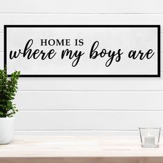 a sign that says home is where my boys are next to a potted plant