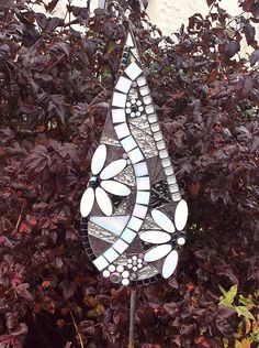 a stained glass wind chime in front of some purple bushes and trees with red leaves