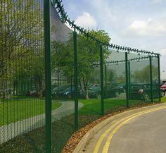 a green fence with barbed wire around it on the side of a road in front of a building