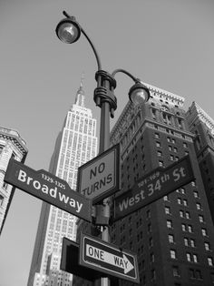 black and white photograph of street signs in new york city with skyscrapers in the background