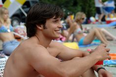 a shirtless man sitting on the beach with his arm around his chest and arms crossed