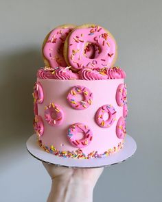 a pink cake with sprinkles and donuts on top is being held by a person