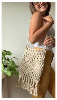 a woman holding a crocheted purse in front of a potted plant and smiling