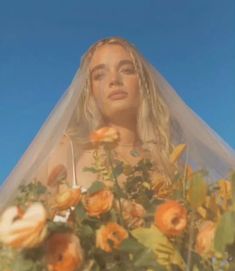 a woman wearing a veil with flowers in front of her face and the sky behind her