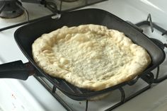 an uncooked pizza sitting on top of a stove next to a frying pan