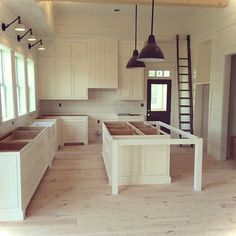 an empty kitchen with wooden floors and white cabinets, ladders hanging from the ceiling