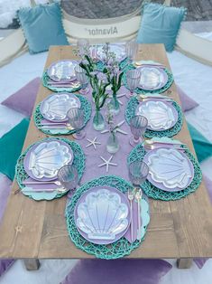 the table is set with purple and blue plates, silverware, and seashells