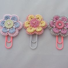 three crocheted flower clips are sitting on a table next to each other and one has a button in the center