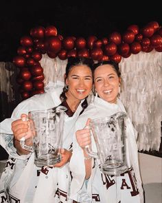 two women are holding large blenders in front of a balloon wall with red balls