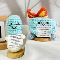 two small crocheted items are displayed on a wooden stand, one is holding a sign