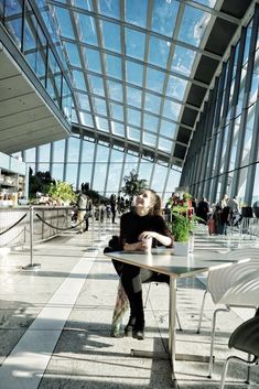 a woman sitting at a table in front of a large glass building with lots of windows