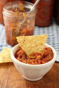 a bowl of salsa with tortilla chips on the side and jar of salsa in the background