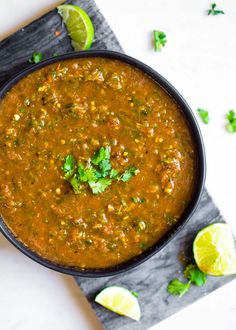 a bowl of chili with limes and cilantro garnish on the side