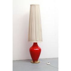 a red table lamp with a white shade on the base and a cord attached to it