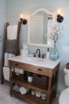 a white toilet sitting next to a bathroom sink under a mirror and a wooden shelf