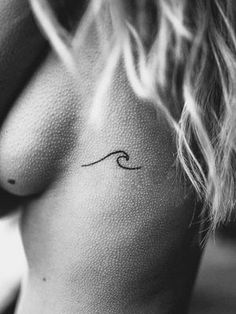 a woman's breast with a small wave tattoo on her left side ribcage