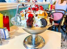 an ice cream sundae on a silver platter with people sitting at the bar in the background