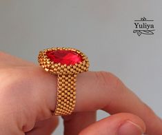 a hand holding a gold ring with a red stone in it's center,