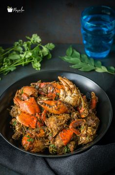 a black plate topped with cooked crabs next to a glass of water and green leaves