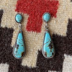 These genuine turquoise and sterling silver handmade dangle earrings are a harmonious blend of elegance and artisan craftsmanship. The focal point of each earring is a mesmerizing turquoise gemstone, displaying its natural beauty with varying shades of greenish blue and hints of earthy matrix, making each piece unique. The turquoise stones are carefully set within sterling silver bezels, enhancing their allure and providing a stunning contrast against the silver backdrop. The intricate detailing of the earrings includes rope borders that gracefully encircle the turquoise stones, adding a touch of texture and sophistication to the design. The dangle style allows the earrings to sway delicately with movement, catching the light and drawing attention to the exquisite craftsmanship. At the top Southwestern Turquoise Earrings With Natural Stones, Turquoise Southwestern Earrings With Natural Stones, Unique Turquoise Teardrop Earrings, Artisan Turquoise Gemstone Earrings, Southwestern Turquoise Drop Earrings, Silver Backdrop, Handmade Dangle Earrings, Faith Jewelry, Earrings Handmade Dangle