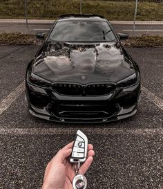 a person holding a car key in front of a black bmw parked in a parking lot