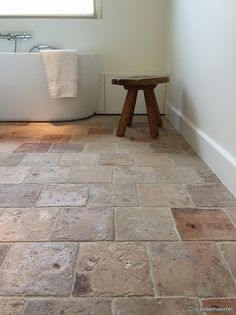 a white bath tub sitting under a window next to a wooden stool in a bathroom